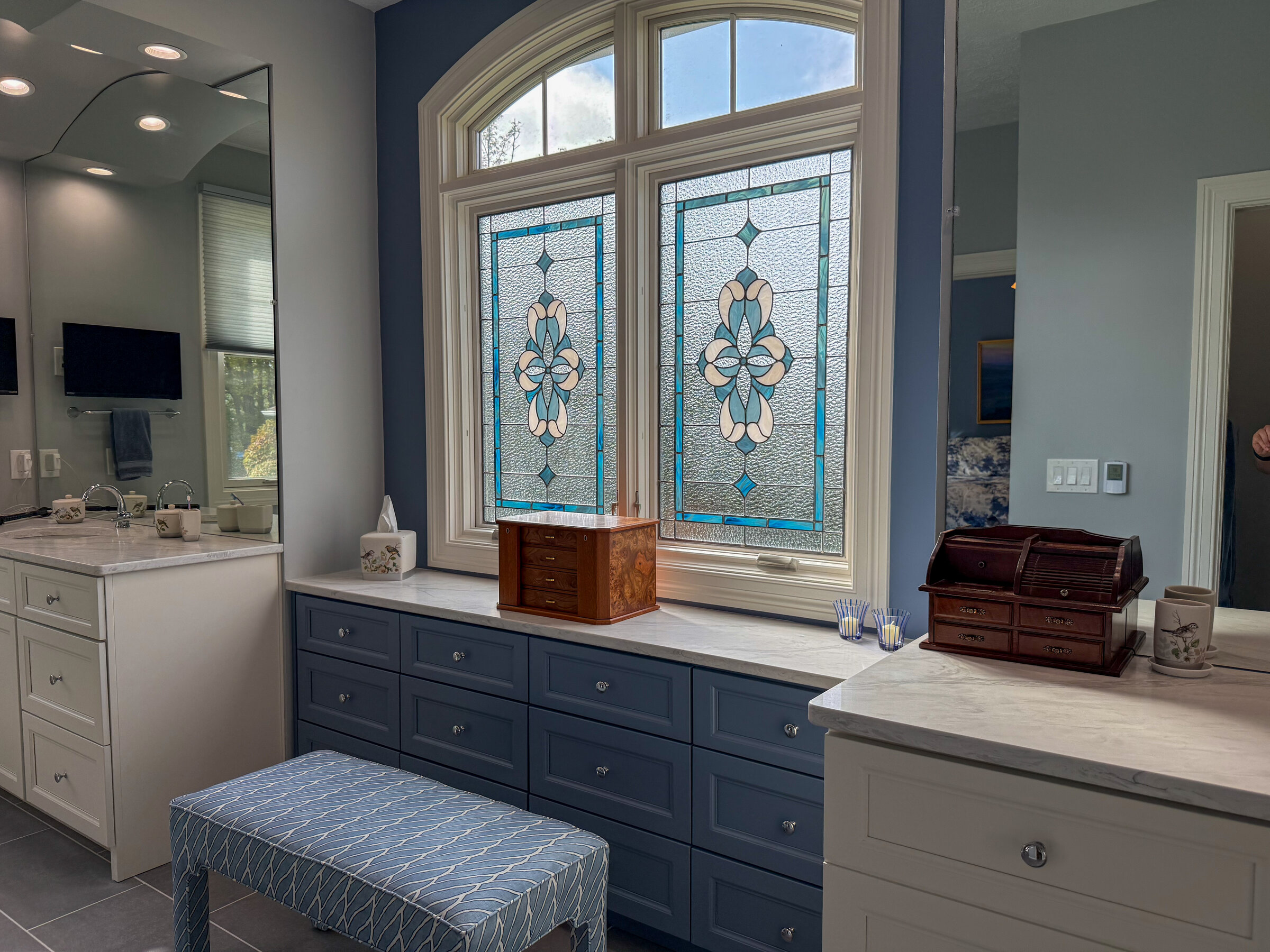Bathroom dressing area with navy blue cabinetry, marble countertops, and custom stained glass window - Marcus Sebastian Renovations