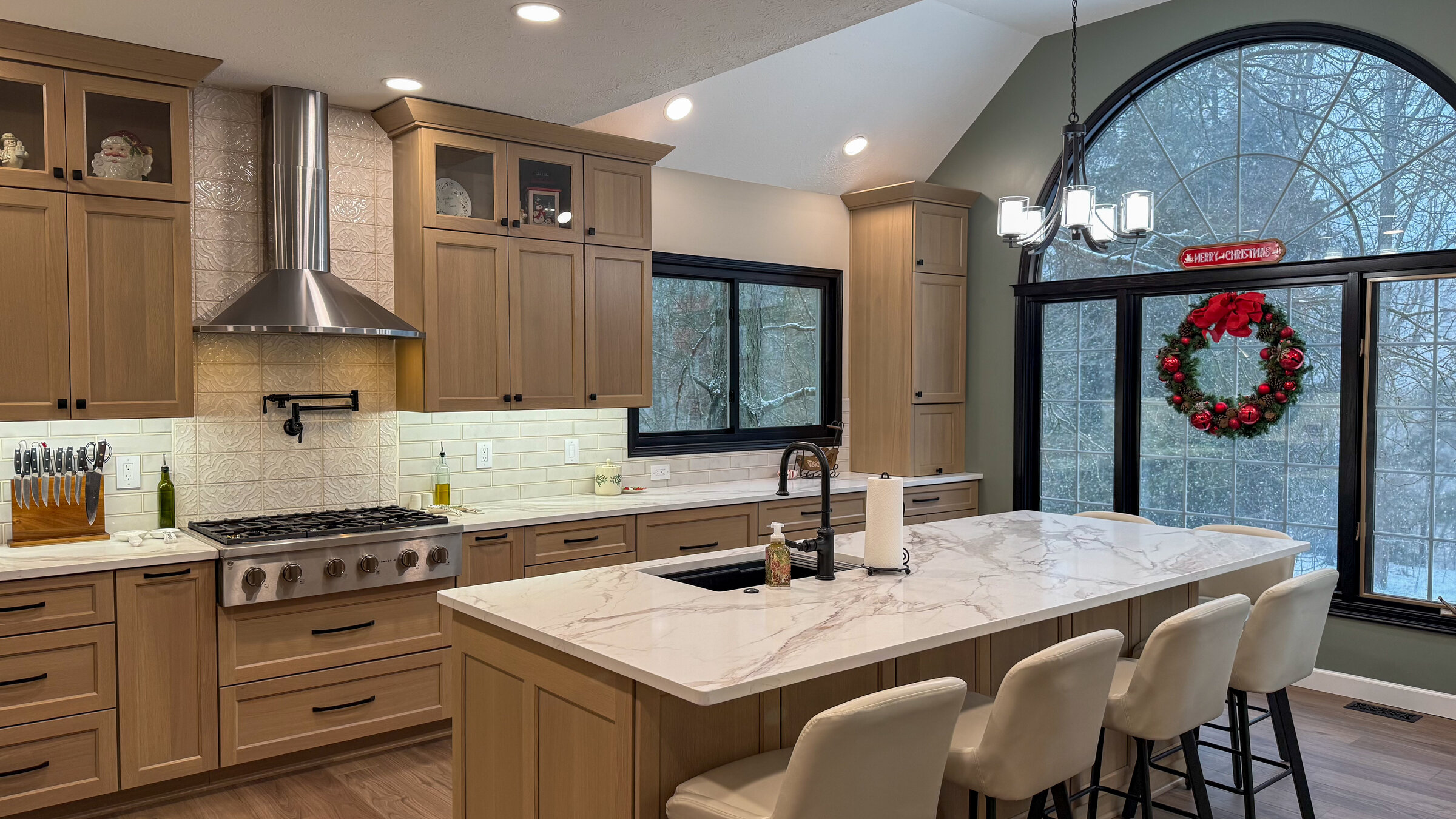 Kitchen remodel with light wood cabinetry, marble waterfall island, and large arched window - Marcus Sebastian Renovations